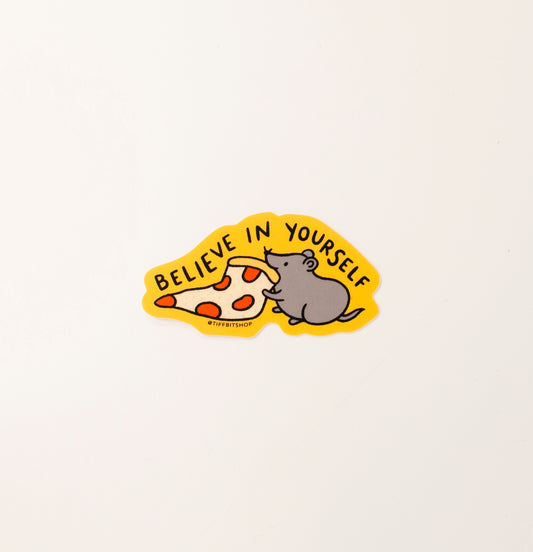 A bright yellow sticker with a drawing of a rat with a slice of pizza in its mouth, the words above read, believe in yourself