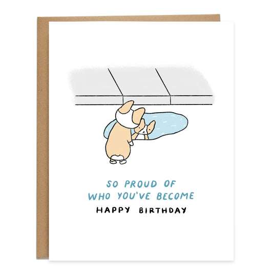 a drawing of a corgi smiling and looking at their reflection in a puddle of water next to the sidewalk, card reads, so proud of who you've become, happy birthday