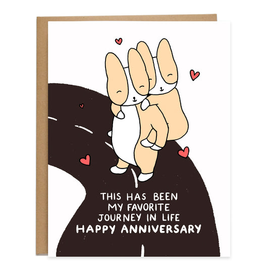 hearts floating around two smiling corgis and one is carrying the other on their back as they're standing on a curving road, text on card reads: this has been my favorite journey in life, happy anniversary