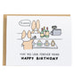 a corgi buying wine and the clerk asking for ID, the card reads, may you look forever young, happy birthday