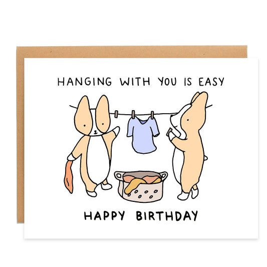 clothing line with a shirt hanging in the background with two corgis hanging clothes, text on card reads: hanging with you is easy, happy birthday