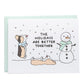 a tricolor corgi jumping up to lick the snow and a tan corgi laying on the ground licking the falling snow with a snowman, card reads, the holidays are better together