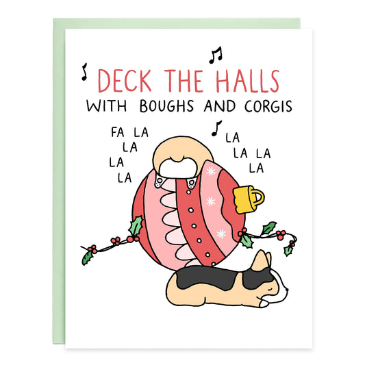 a corgi falling over a large red ornament and a tricolor corgi asleep on the floor, the card reads, deck the halls with boughs and corgis