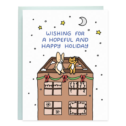 a drawing of a winter scene with a corgi and orange tabby sitting on the roof of a building with the stars and crescent moon above with the cat pointing up at words that read wishing for a hopeful and happy holiday, with snow falling around them