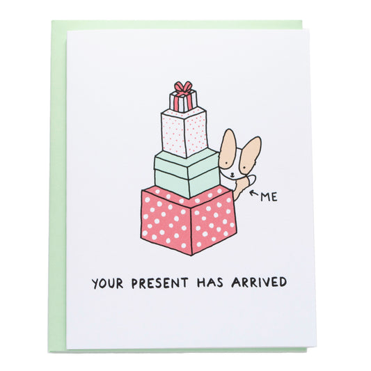 the card reads, your present has arrived. a corgi peeking out from a tower of large presents, there's an arrow pointing at the corgi that reads, me