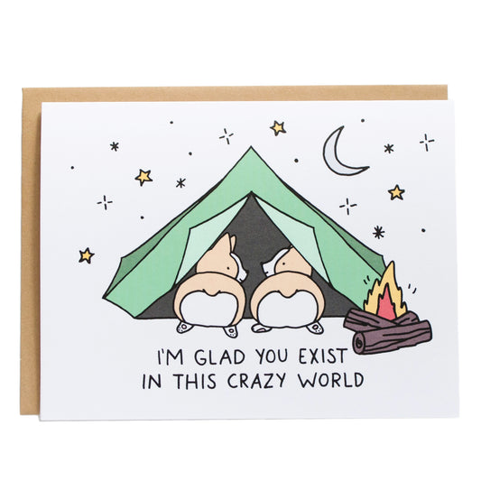 two corgis laying in a green tent camping under the stars with a fire burning, card reads, i'm glad you exist in this crazy world