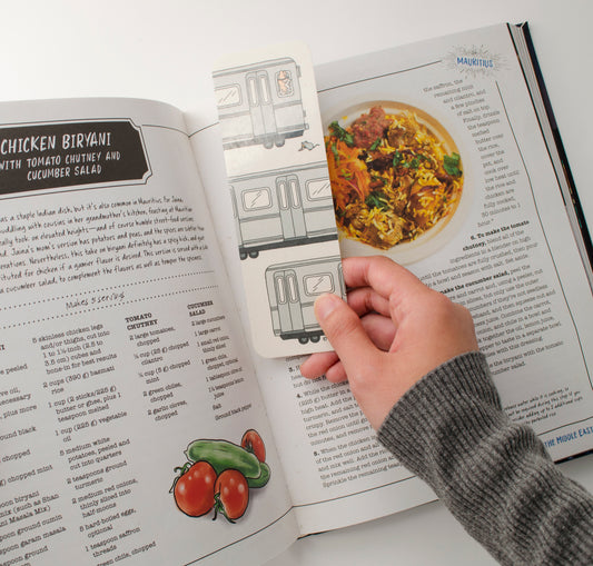 A cookbook open to a chicken biryani recipe and a hand holding the bookmark to the middle of the book