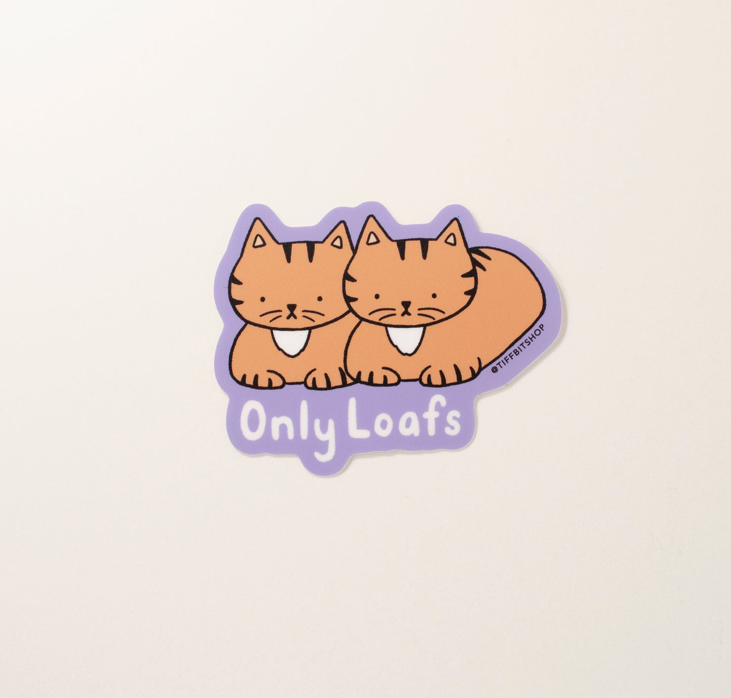 On a purple background, a drawing of two brown tabby cats in a bread loaf position. On the bottom, in white bubbly text it reads, OnlyLoafs